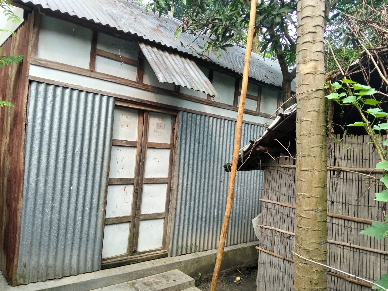 Tin house with a panelled wooden double door, a bamboo fence at the side.